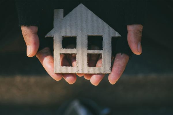 photo de mains avec des gants abimés portant une maison en carton